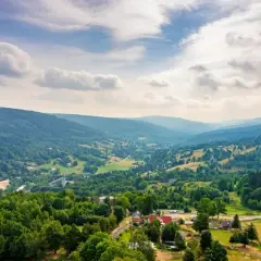 Malowniczy krajobraz Gór Izerskich z zielonymi wzgórzami, lasami i kilkoma domami.
