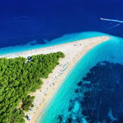 Zloty piasek i turkusowa woda na chorwackich plażach. W oddali widać łódź motorową.