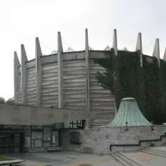 Monumentalny budynek Panoramy Racławickiej, częściowo porośnięty bluszczem, z charakterystycznym betonowym dachem i wejściem.