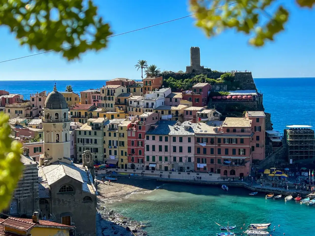 Kolorowe domy Cinque Terre wznoszą się nad turkusowym morzem, z wieżą strażniczą na wzgórzu.